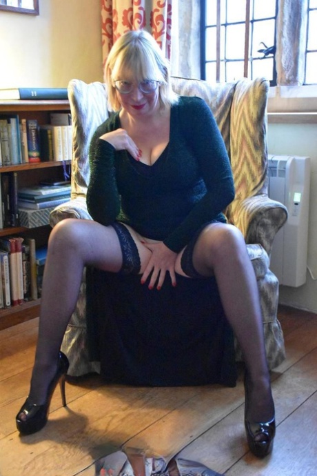 Barby Slut, an older woman of blonde appearance, displays her genitals on a chair during upskirt action.