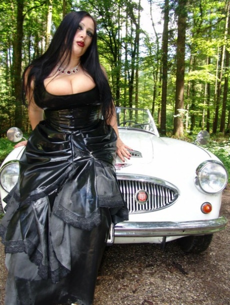 Goth Lady Angelina loses her large breasts while sitting on a car in the woods.