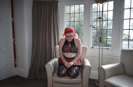 Mollie Foxxx, the big red cat, uses her thick fingers and toys to suck her penis while sitting on a chair.