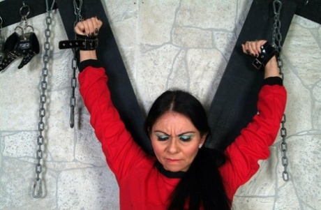 This picture shows a girl with black hair who is fully clothed and attached to a St Andrew's Cross.