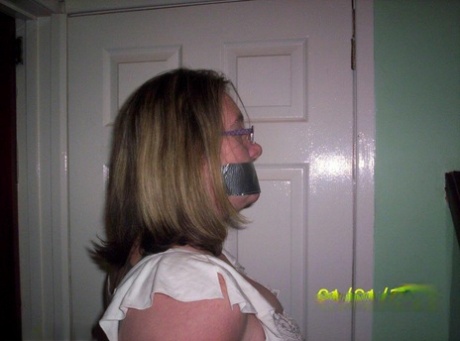 Caucasian female displays her natural tits as she is gagged and tied down by rope.