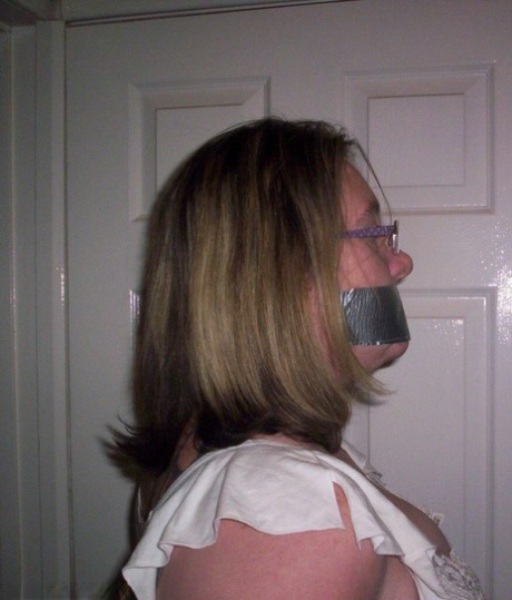 Caucasian female displays her natural tits as she is gagged and tied down by rope.