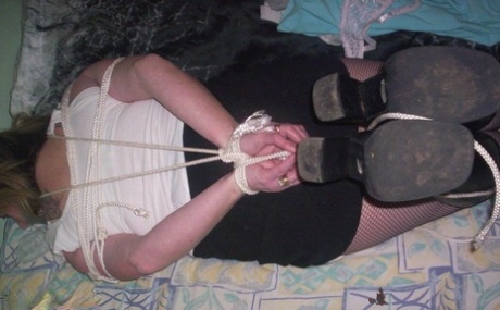 White woman displays her natural tits as she is gagged and tied down by a rope.