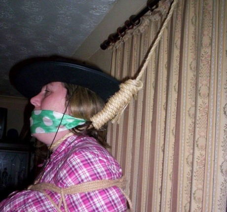 A female household guest is observed holding her big tits in the middle of a bedroom, while being gagged and nooted.