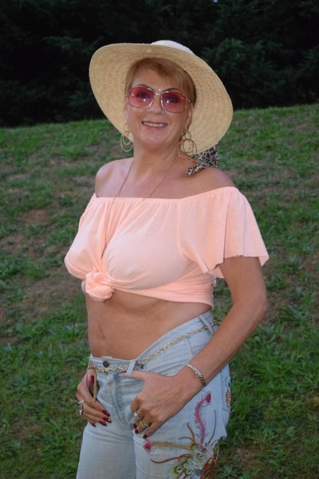 Aged female Dimonty removes her clothes in a backyard and wears sunglasses.