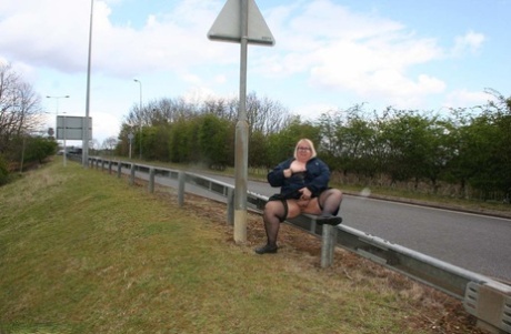 Lexie Cummings, an Obese UK blonde, pees on a concrete block situated beside a road.