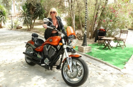 Atop a motorcycle, the adult blonde Melody displays her sizable breasts.