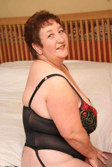 The overweight British woman, Kinky Carol, displays her substantial chest and thighs on a bed.