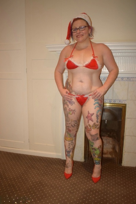 An elderly woman with tattoos gets away with a nude bikini pose and a Santa cap.