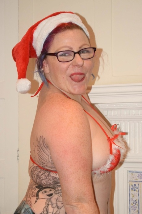 Older female with tattoos gets naked in a bikini pose while wearing her Santa cap.