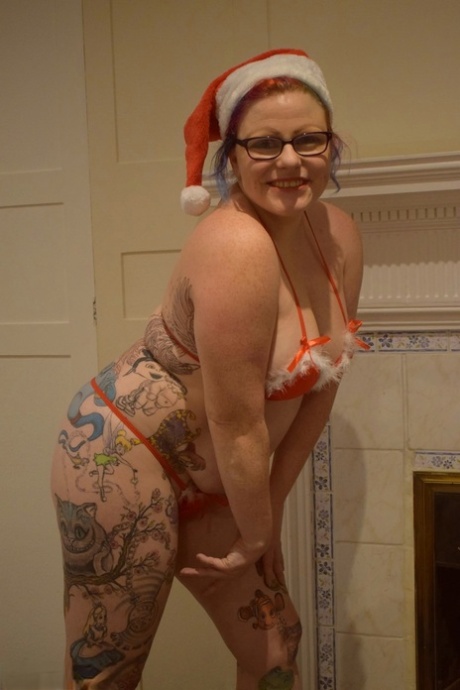 An elderly lady with a tattoo gets away with a nude bikini pose and a Santa cap.