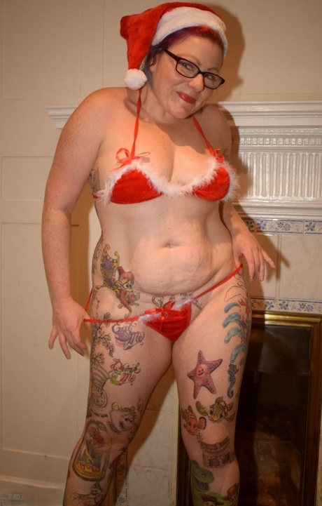 The older woman who has a tattoo removes her nude Santa cap while in a bikini pose.