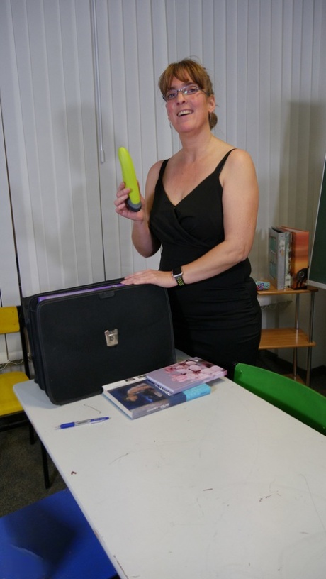 Aged teacher Marie R wears glasses and red heels as she masturbates at her desk.