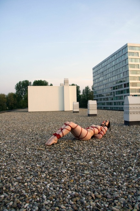 The naked brunette is left alone on a rooftop tied up with red rope.