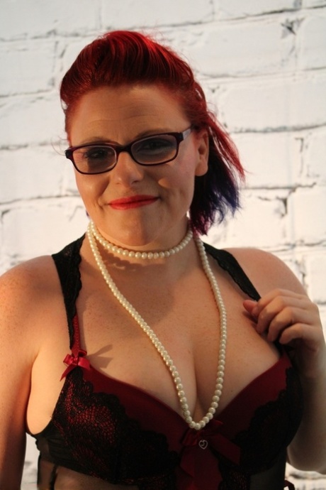 The chubby redhead, who wears glasses and nylons, loosens her tits from lingerie.