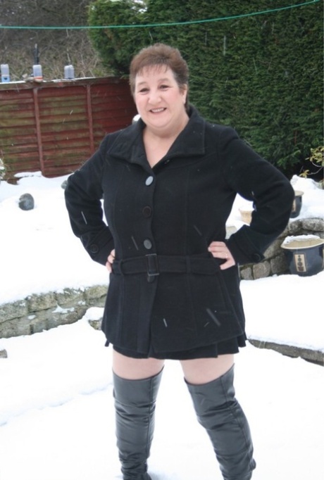 Snow-covered ground causes Kinky Carol, an aged UK fatty, to strip down in over the knee boots.