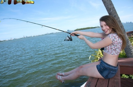 Adolescent girl Elena Koshka lays out her small breasts while fishing from the shore.