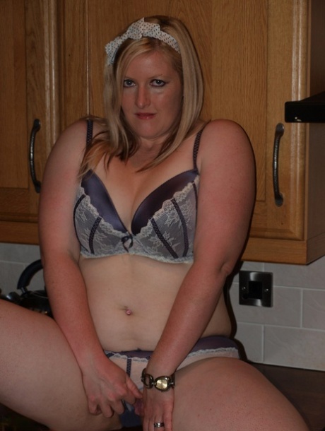 In a kitchen, Samantha, a blonde who is overweight, grabs her pen and covers her body with her legs.