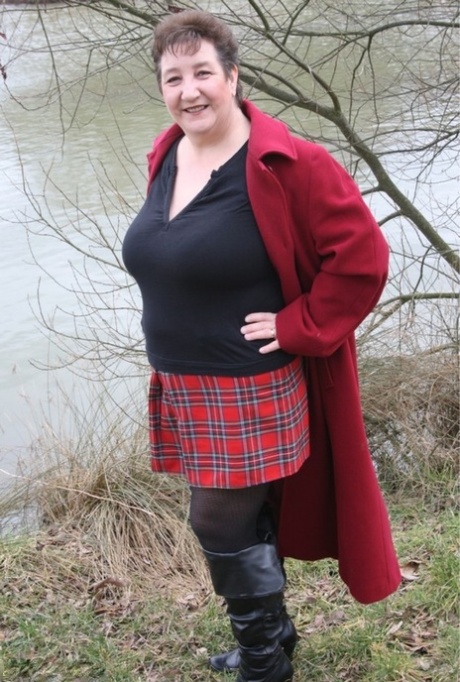 Kinky Carol, a fat woman from the UK, removes her shirt near the water while wearing a plaid skirt.