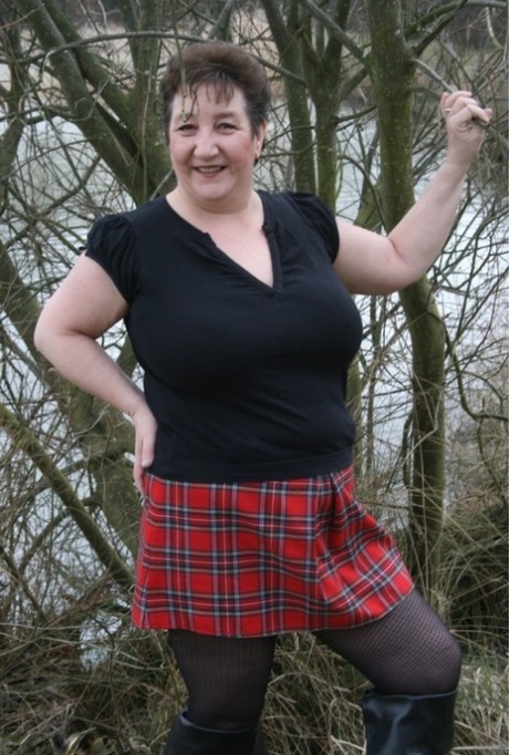 A fat UK girl named Kinky Carol removes her shirt while wearing a plaid skirt near the water.