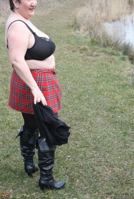 A plaid skirt is worn by a fat UK woman, Kinky Carol, who removes her shirt near the water.