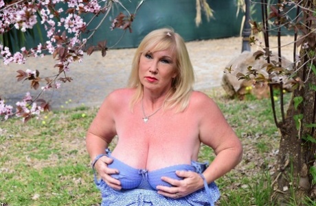While in a yard, the mature blonde Melody exposes her large breasts.