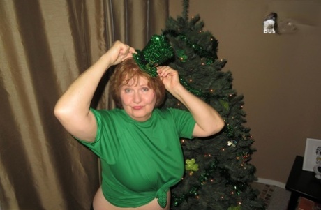 Busty Bliss the adult Irish plumper stands in front of a Christmas tree and goes without clothes.