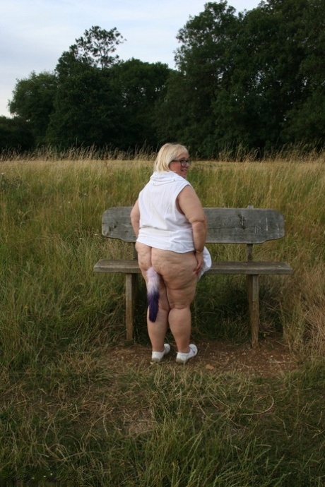 On a bench in a field, Lexie Cummings, a plump British woman, exposes herself.