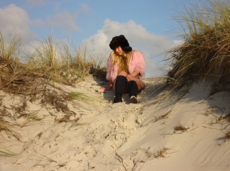 Shaggy blonde Luscious Models don her black boots for a nude walk on a beach.