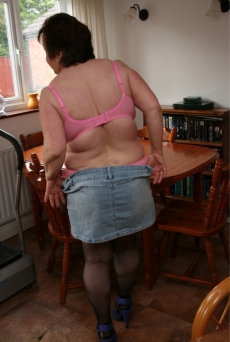 While stripping off in a bra and miniskirt, Kinky Carol, an older British fat woman, is seen at a table.