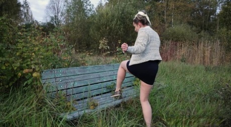 Black woman Katy Dee climbs up a black miniskirt before peeing on the bench.