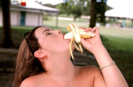Thick chick Annie Swanson eats a banana before baring her breasts in a park