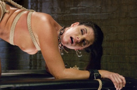 Brunette MILF is subjected to flogging and penetration while being restrained in a dungeon.