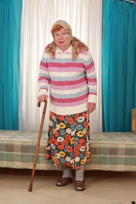 Fat and old granny Alice with a cane, fully dressed in a long skirt and socks.