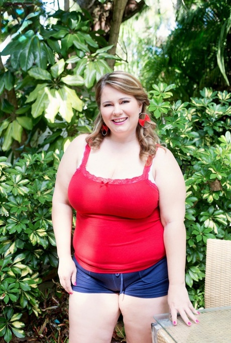 A photo features blonde BBW Cj Woods stripping down to her bra in denim shorts as she walks on the patio.