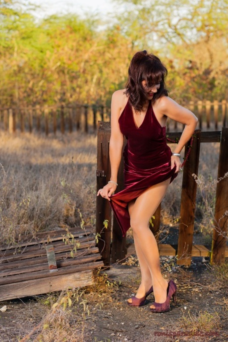 A naked woman named Roni Ford takes off her velour dress for nude outdoor poses.