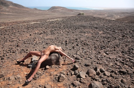 Thin teen Maria fingers her tight twat after posing nude on rock in wastelands