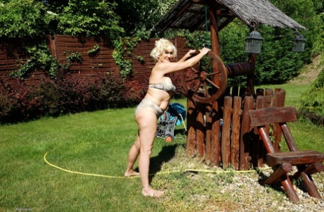 The older, blonde woman removes her bikini while walking around the house.