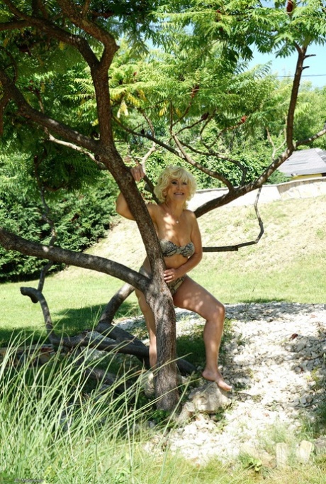 A fully-grown blonde woman takes off her swimsuit while exploring the area around her home.