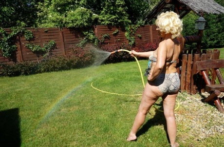 A blonde woman of long-term status removes her bikini while walking around her house.