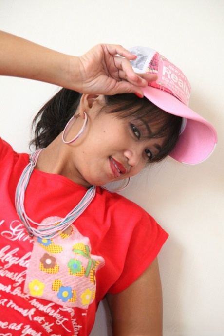 An Asian girl exhibits her beaver in a T-shirt and ball cap.