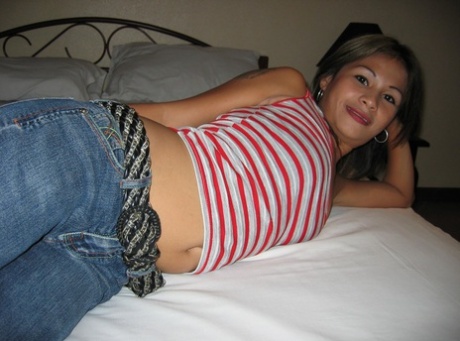 The Pinay bargirl removes her shirt to take a picture on a bed, wearing a strapless bra and jeans.