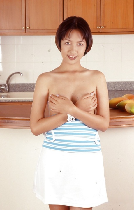 In the kitchen, a young Asian in revealing clothing with tiny tits is seen with legs covered with spreads.