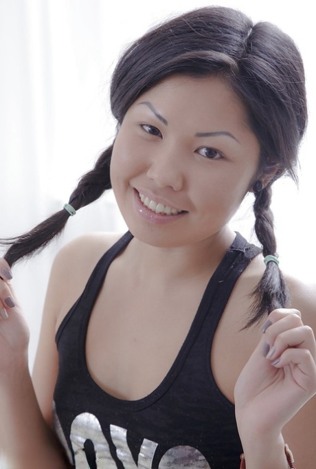 To reveal small tits, the Asian beauty with pigtails pulls on her blouse over her head.