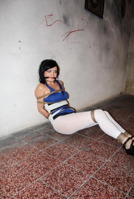 The girl with dark hair is gagged and tied up in rope, leaving her helpless.