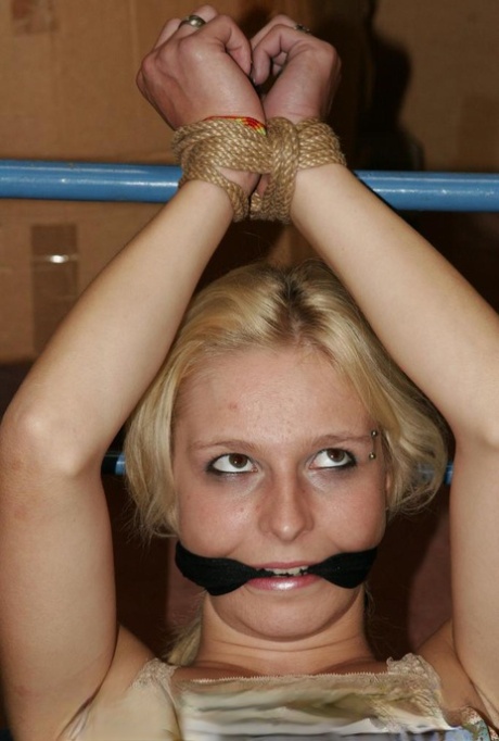 With her wrists fastened to a bed frame, Ilona, the gorgeous blonde, is having difficulty getting past a machine dildo.