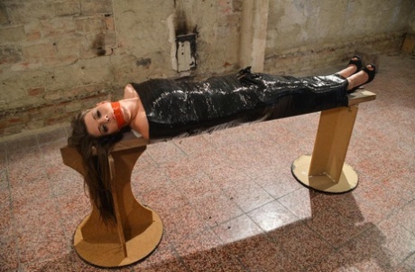 The naked female, wearing high-heeled shoes, is covered in plastic and has a gagged appearance.