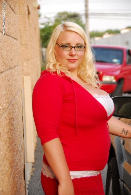 A fat blonde woman with glasses smoking and removing her clothes.