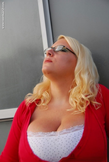 With glasses on, a fat blonde woman was smoking and taking off her clothes.