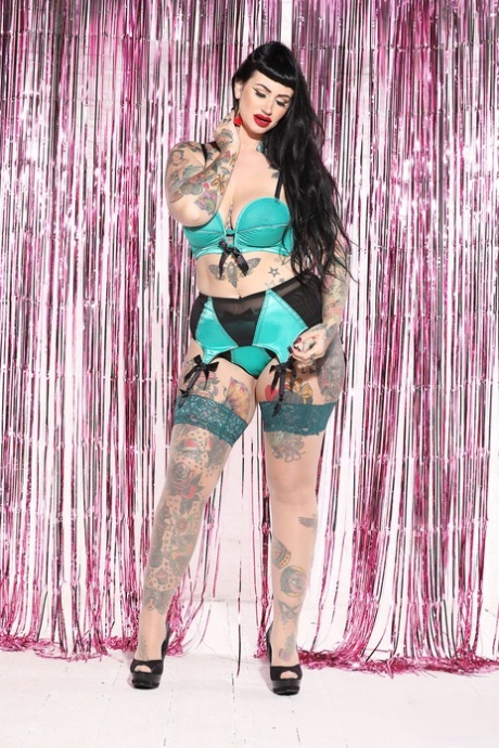 In lingerie worn over her bust, Lucy Vixen showcases the full figure of a voluptuous tattooed model.